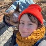 Person in bright orange beanie smiling at the camera with a mid-size dog.
