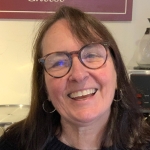 Woman with brown hair and glasses smiles at camera.