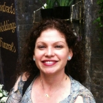 woman with wavy shoulder-length dark brown hair, small blue earrings, holding a sub sandwich